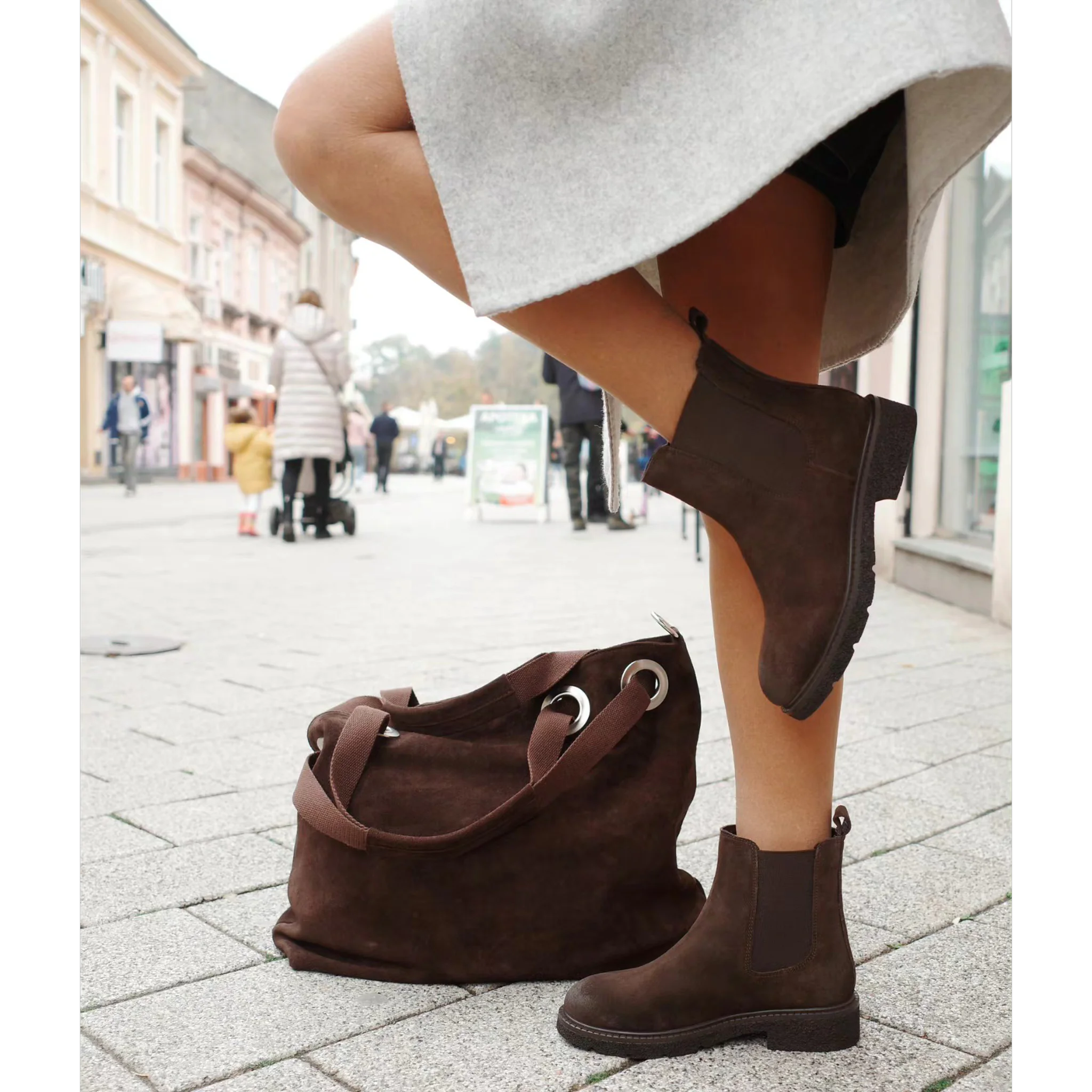 Woman wearing brown Chelsea boots with zip closure and matching brown suede handbag on city street