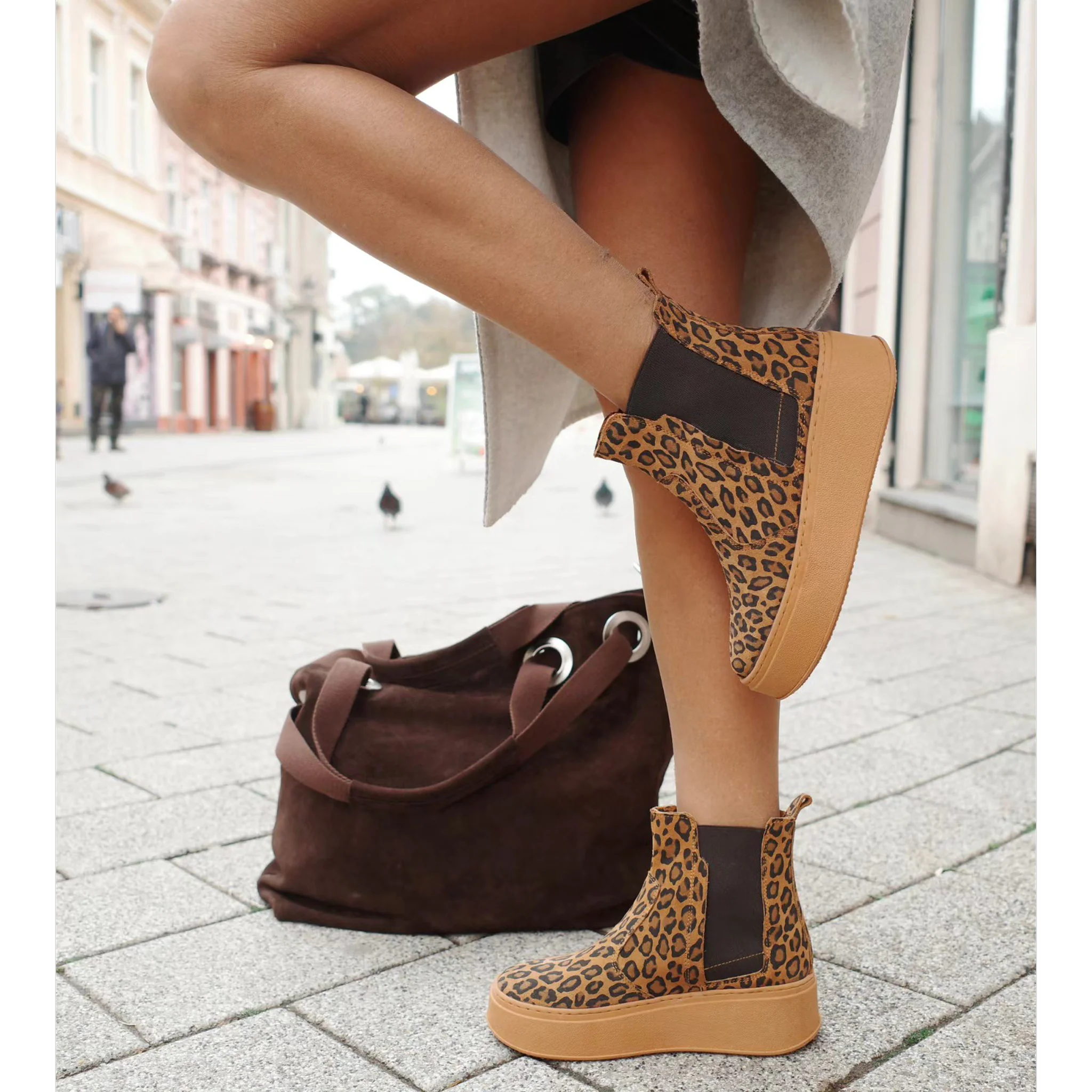 Close-up of leopard print Chelsea platform boots worn by person, with brown suede bag on pavement