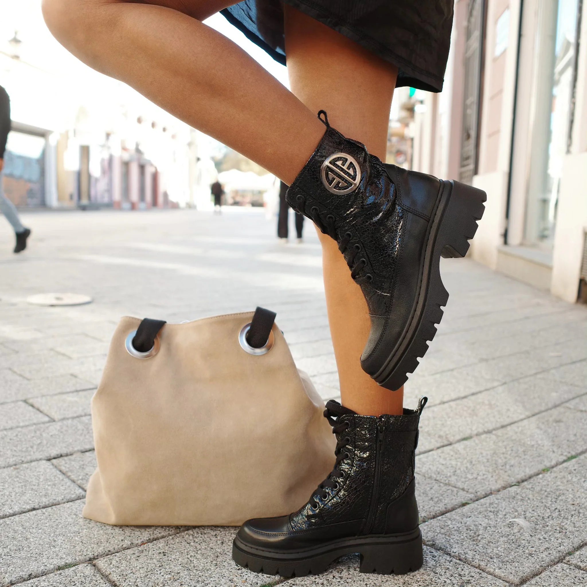 Black short straight leather combat boots with zip and logo detail worn with a beige bag on city street