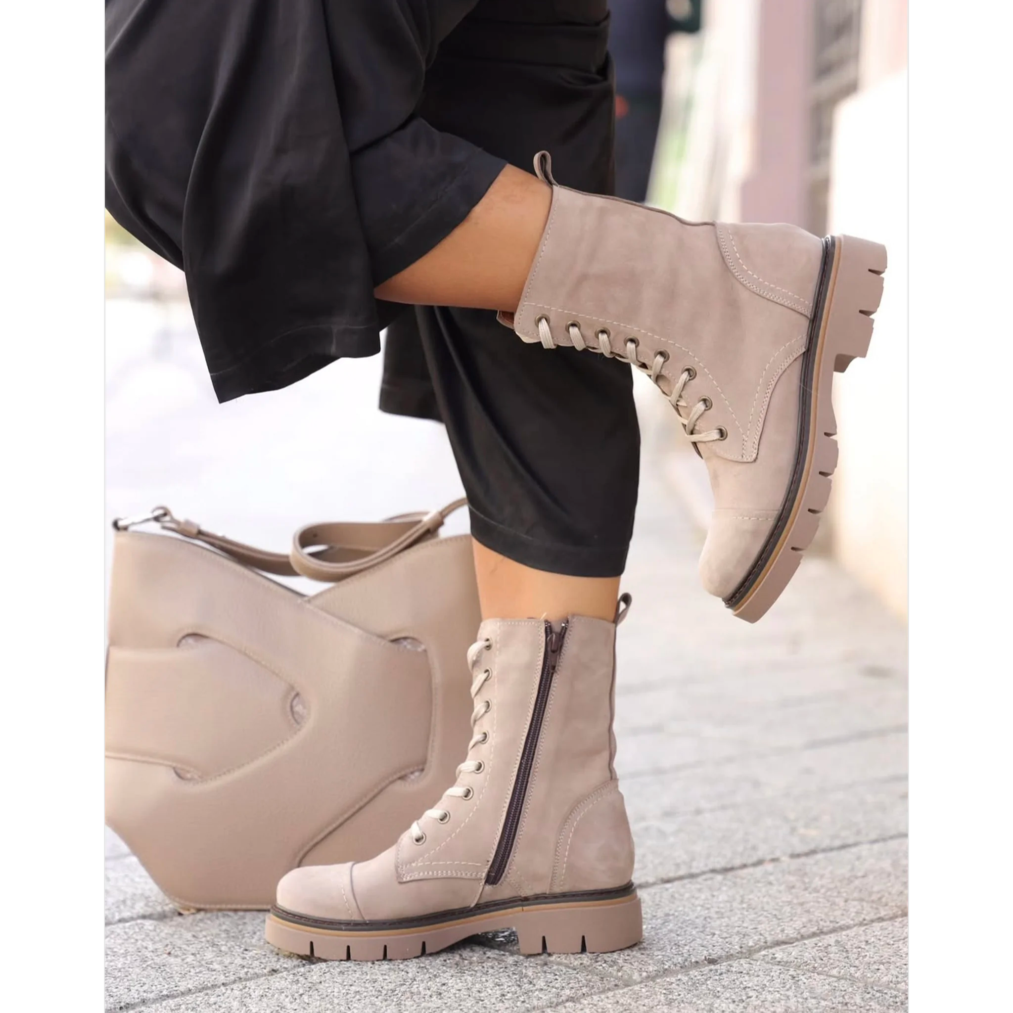 Taupe lace-up combat boots with side zipper worn with black pants, taupe handbag on pavement