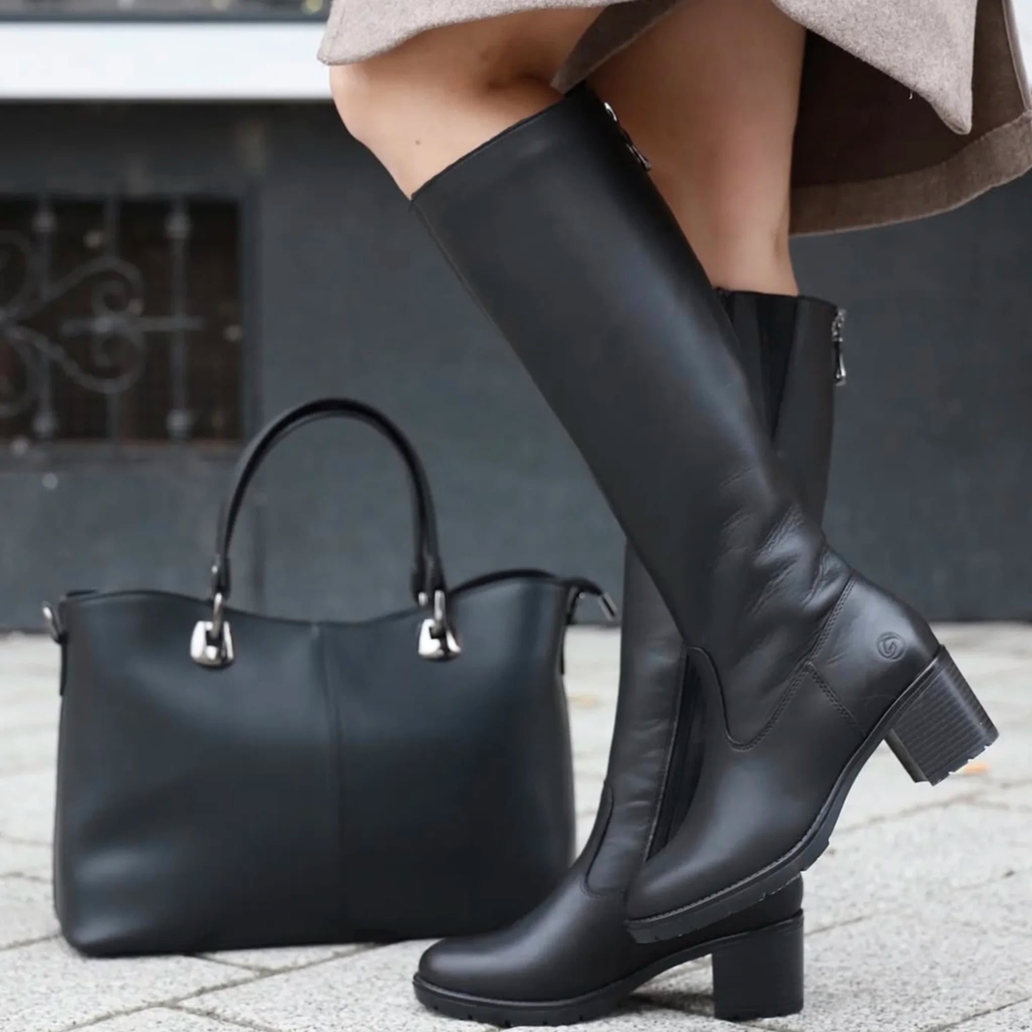 Black knee-high leather boots with block heels and zipper, paired with black leather handbag on pavement