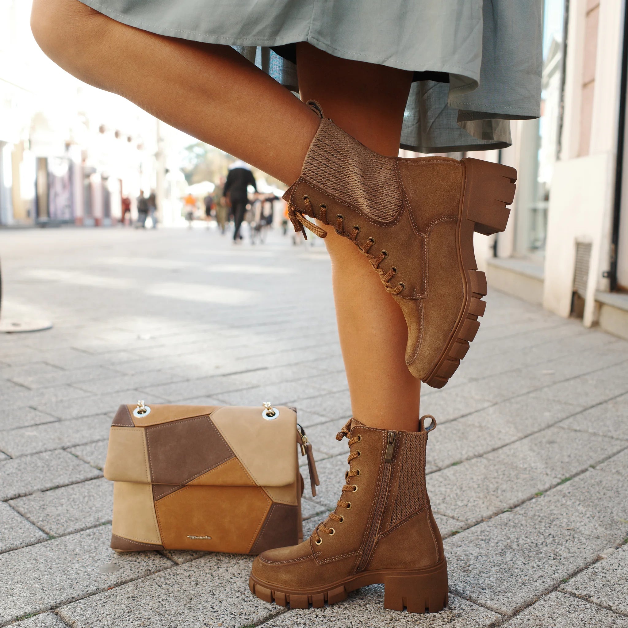 brown lace-up ankle boots with zipper worn by a person standing on a street next to a patchwork leather handbag