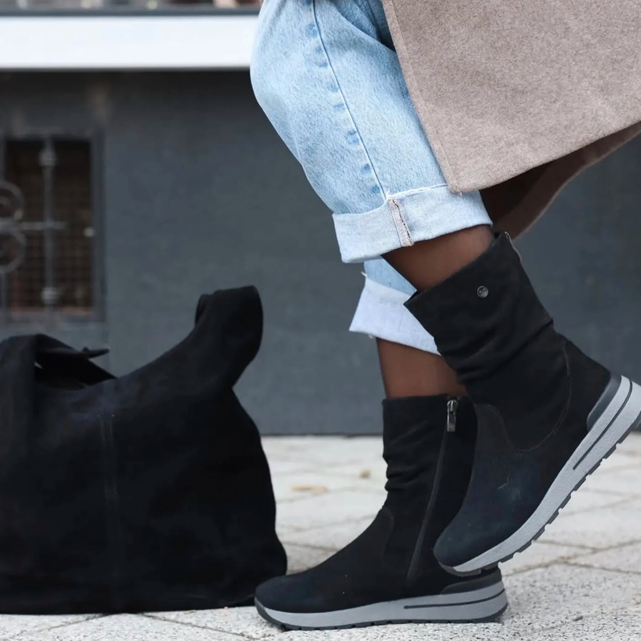 Black suede mid-calf boots with side zipper worn with cuffed light blue jeans outdoors