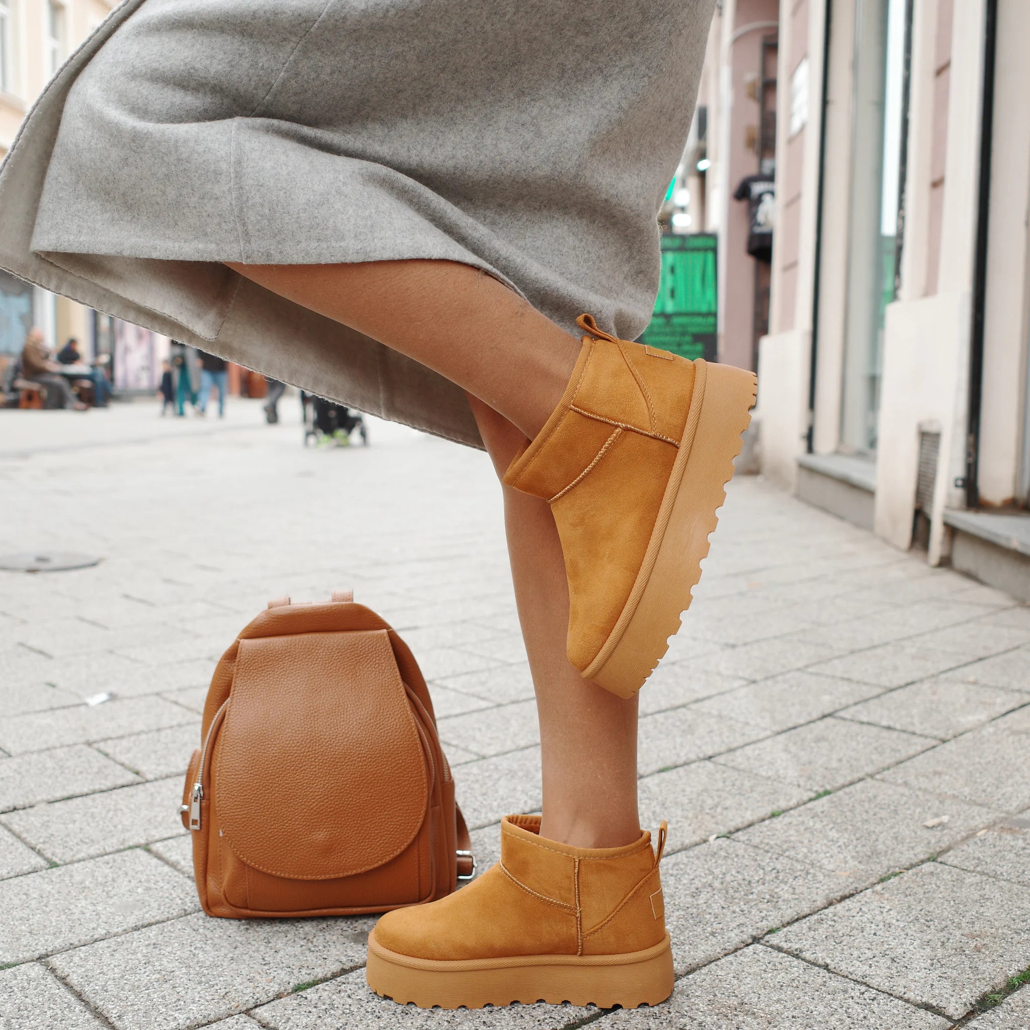 Person wearing ocher platform ankle boots with brown leather backpack on city street