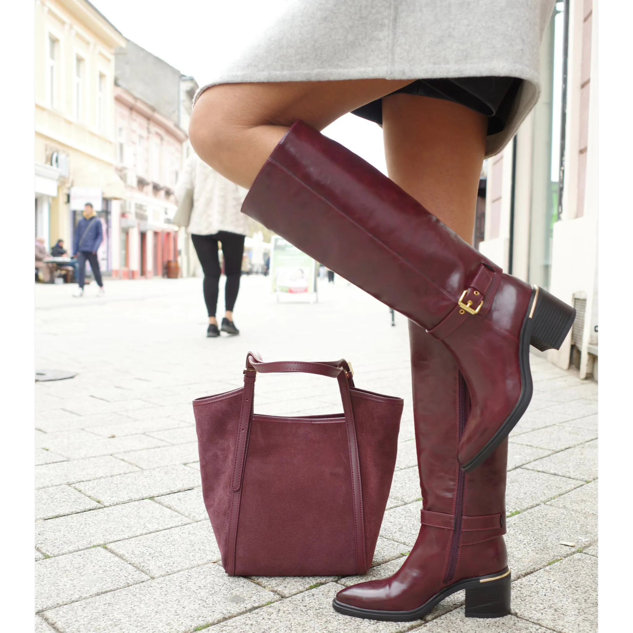 Woman wearing burgundy knee-high leather boots with block heels and matching suede handbag on city street