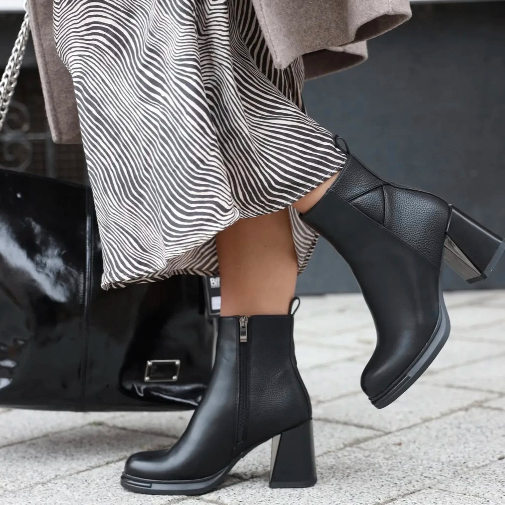 Black leather ankle boots with chunky heels and side zippers worn with a striped skirt and beige coat