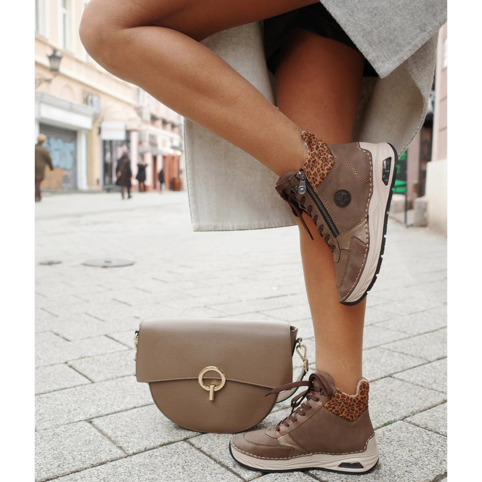 Close-up of woman wearing brown Rieker ankle boots with leopard print collar and beige handbag on city street